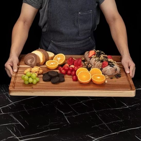personne tient planche à découper bois avec fruits et pain